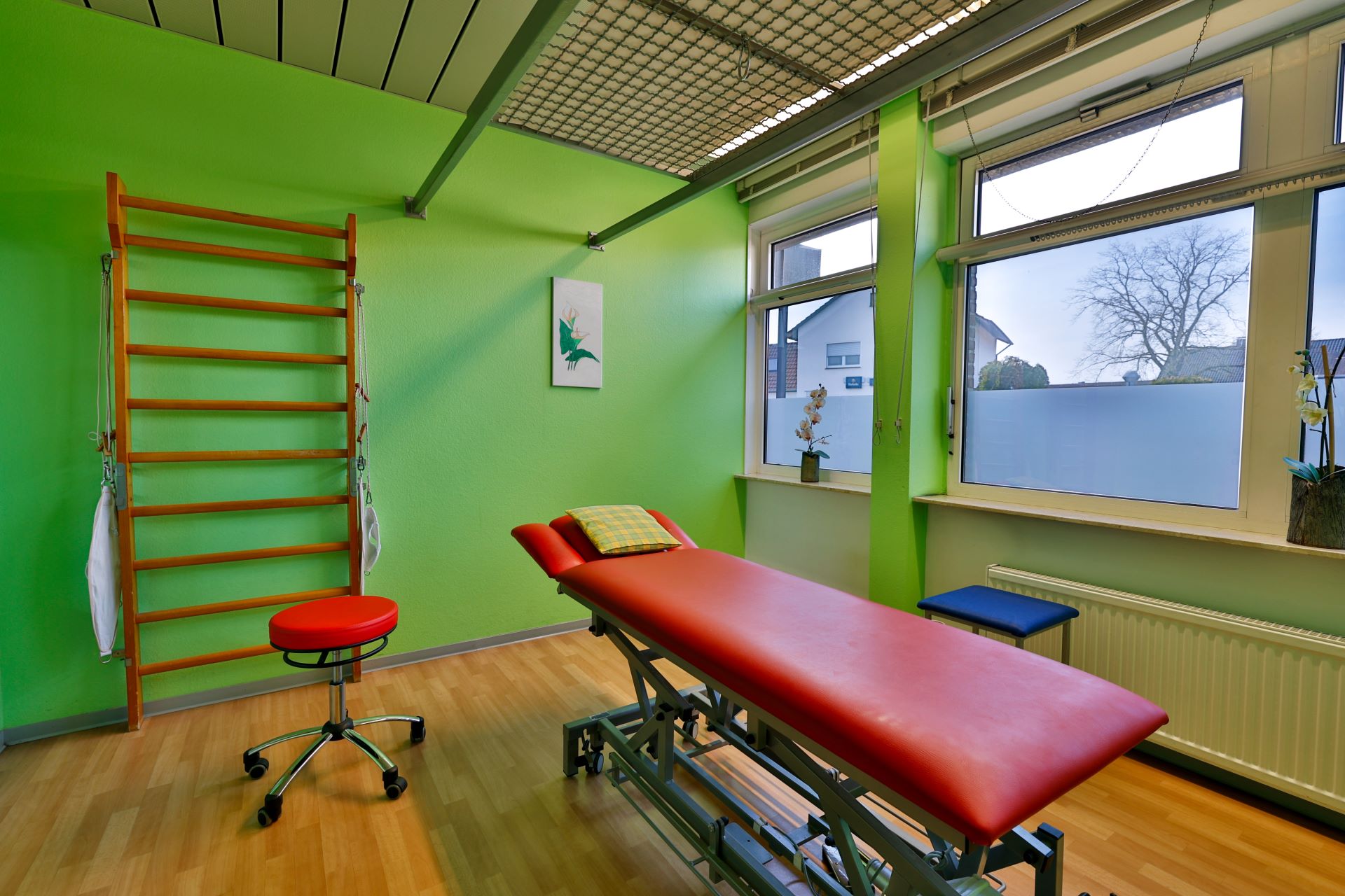 Heller Therapieraum mit grün gestrichenen Wänden, roter Liege und Holzsprossenwand