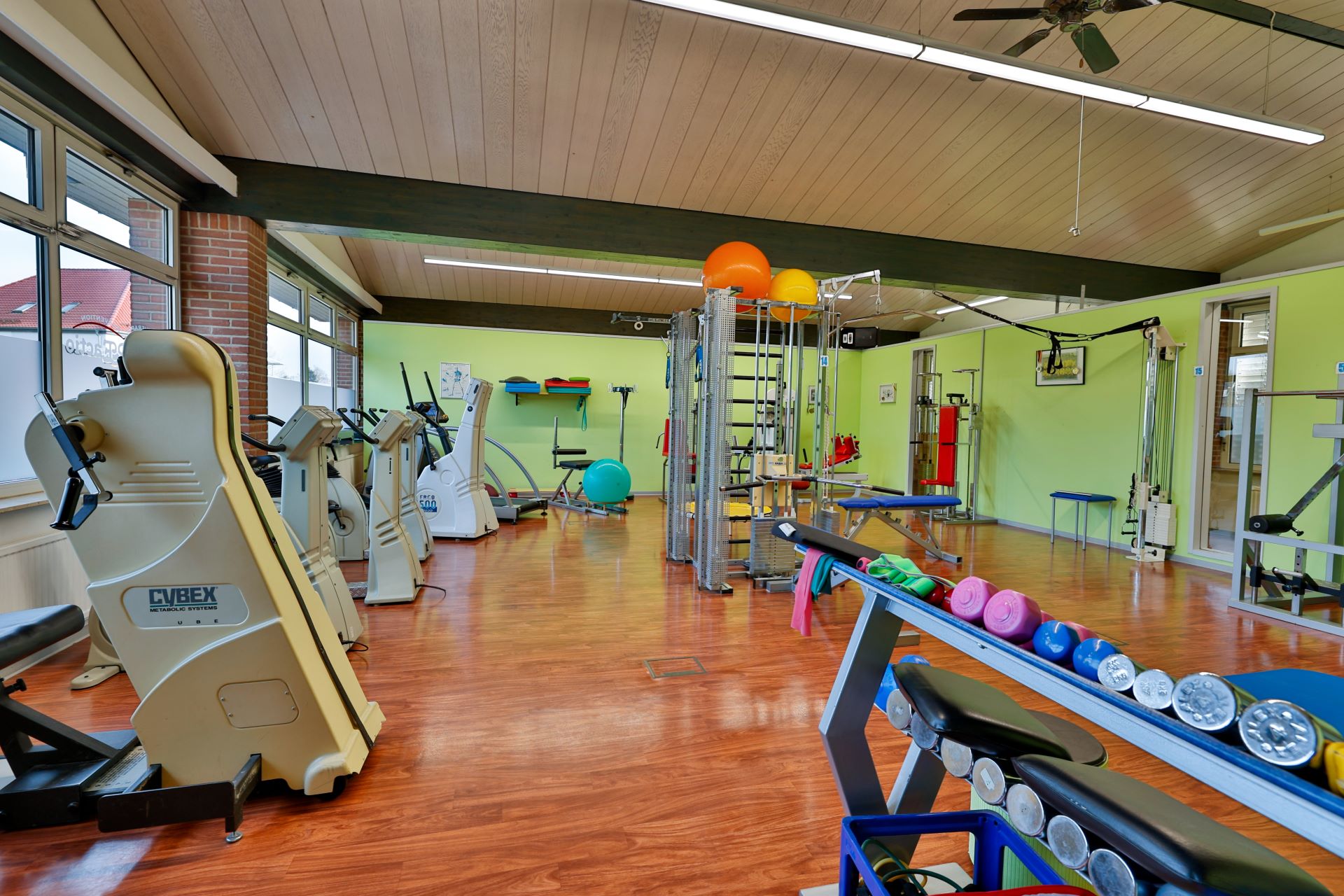 Heller Fitnessraum mit bunten Hanteln und modernen Trainingsgeräten auf Holzfußboden