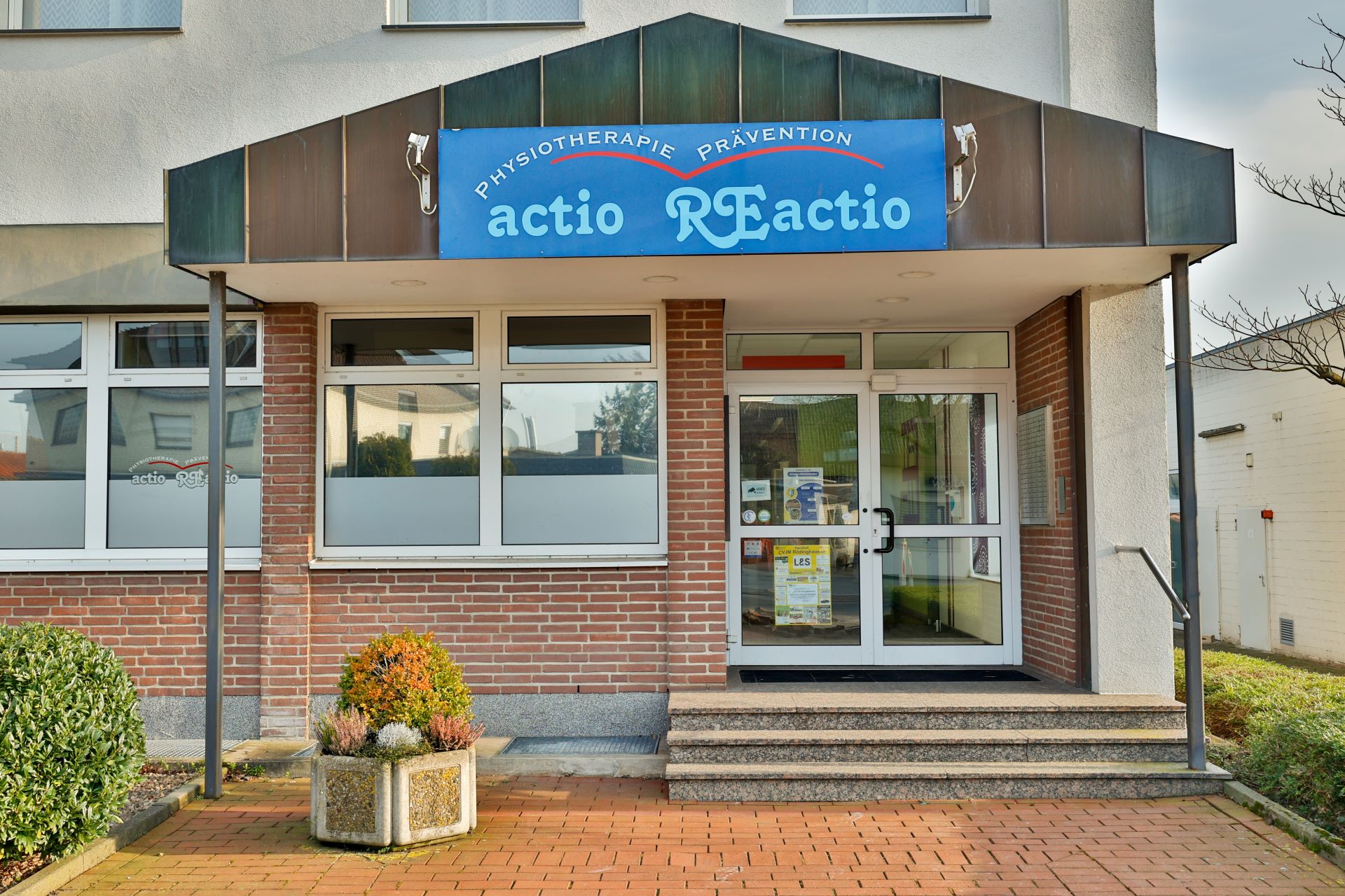 Der Eingang einer Physiotherapiepraxis mit blauem Schild und reflektierenden Fenstern