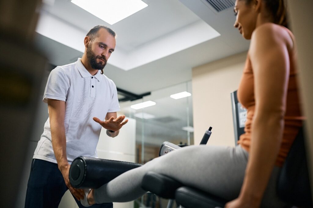 Ein Personal Trainer hilft einer Sportlerin bei ihrer Rehabilitationsbehandlung im Fitnessstudio.