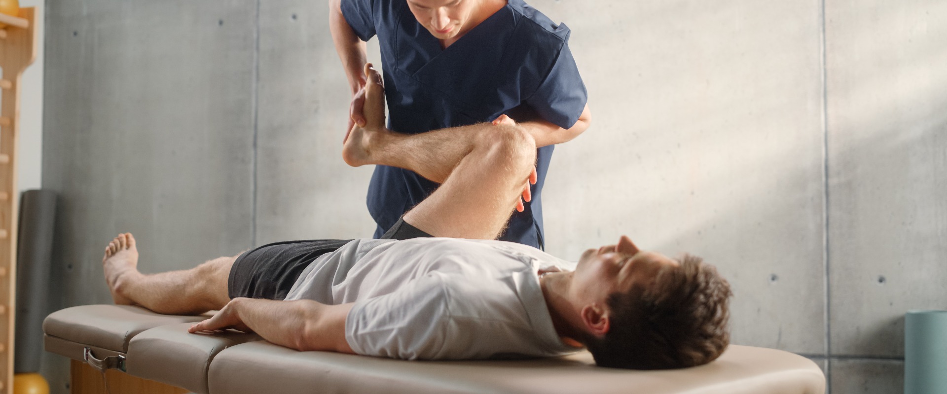 Fortgeschrittene Sportphysiotherapeutin beim Dehnen und Arbeiten an Muskelgruppen oder Gelenken mit einem jungen männlichen Athleten. Ein fitter Sportler, der sich von einer leichten Verletzung erholt und sich in der Rehabilitation befindet.