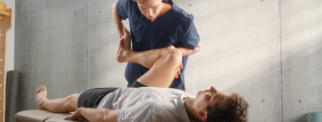 Fortgeschrittene Sportphysiotherapeutin beim Dehnen und Arbeiten an Muskelgruppen oder Gelenken mit einem jungen männlichen Athleten. Ein fitter Sportler, der sich von einer leichten Verletzung erholt und sich in der Rehabilitation befindet.