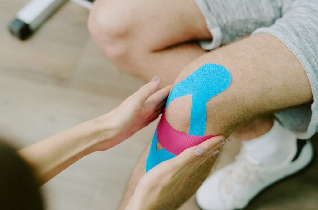 Physiotherapeut beim Anlegen von Kinesio-Tapes am Knie