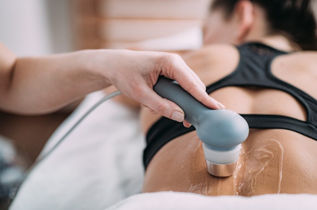 Ultraschall in der Physiotherapie. Therapeut bei der Anwendung eines Ultraschallgeräts am unteren Rücken eines Patienten.